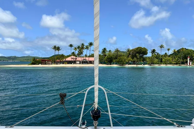Dignity Yacht Photos Pics Lagoon 50 catamaran sailing near tropical island with palm trees and clear blue sky.