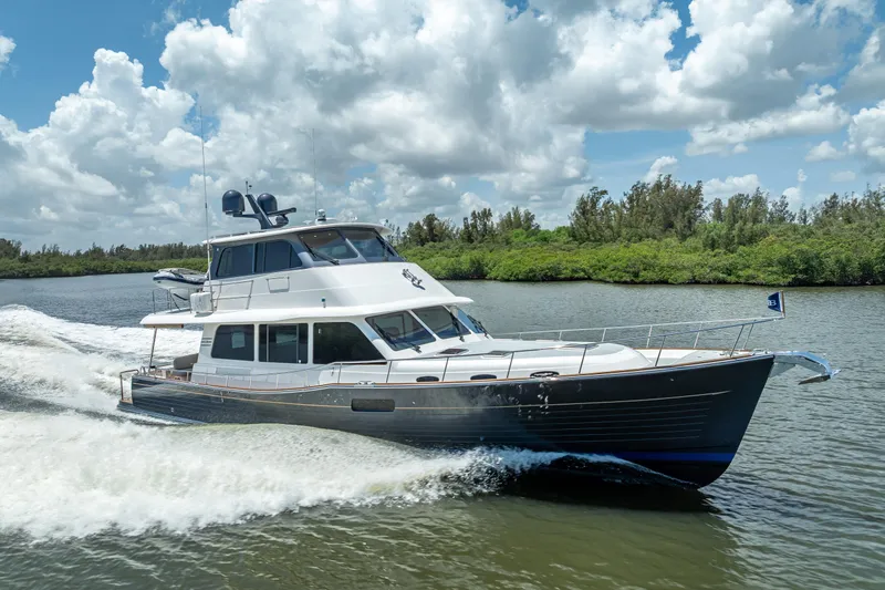 Escape Yacht Photos Pics 2022 Grand Banks GB60 Skylounge yacht cruising on a scenic waterway under a cloudy sky.