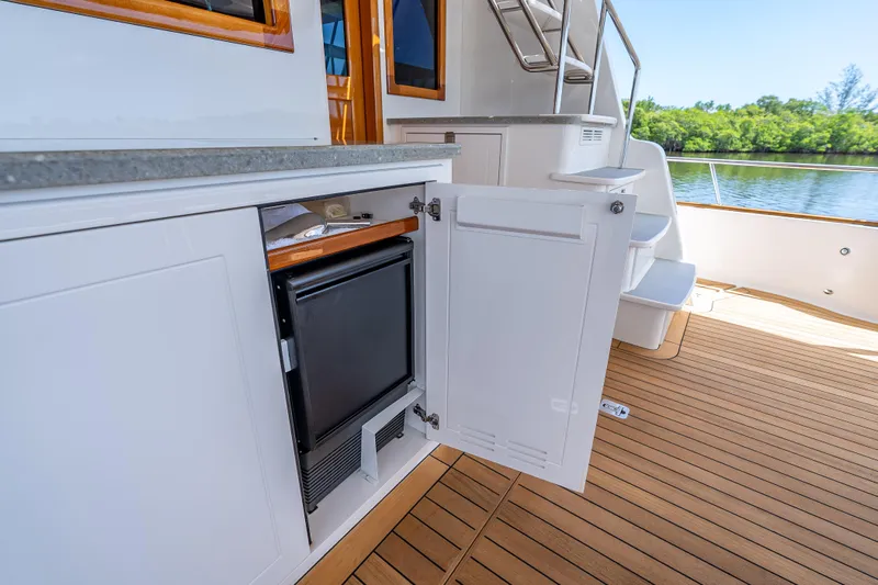 Escape Yacht Photos Pics 2022 Grand Banks GB60 Skylounge yacht with open cabinet and mini fridge on teak deck.