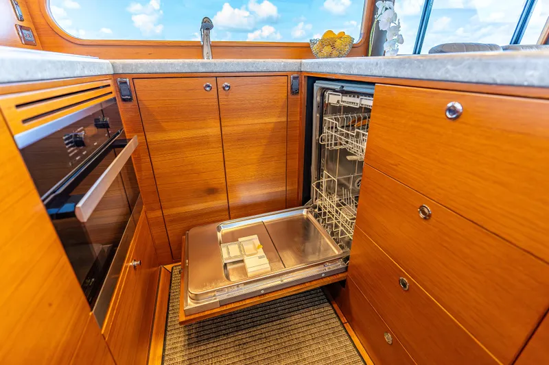 Escape Yacht Photos Pics Luxurious 2022 Grand Banks GB60 Skylounge kitchen with open dishwasher and wooden cabinetry.