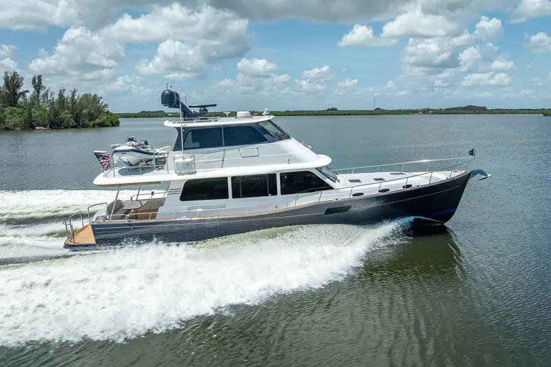 Escape Yacht Photos Pics 2022 Grand Banks GB60 Skylounge yacht cruising on a serene waterway under a cloudy sky.