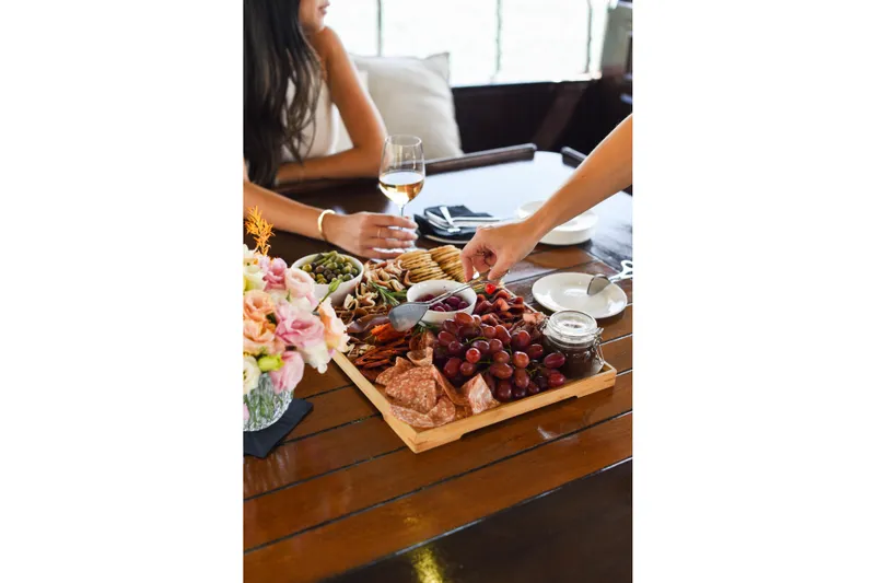 Gaiole Yacht Photos Pics Charcuterie board with grapes, meats, and crackers on a wooden table, accompanied by wine.