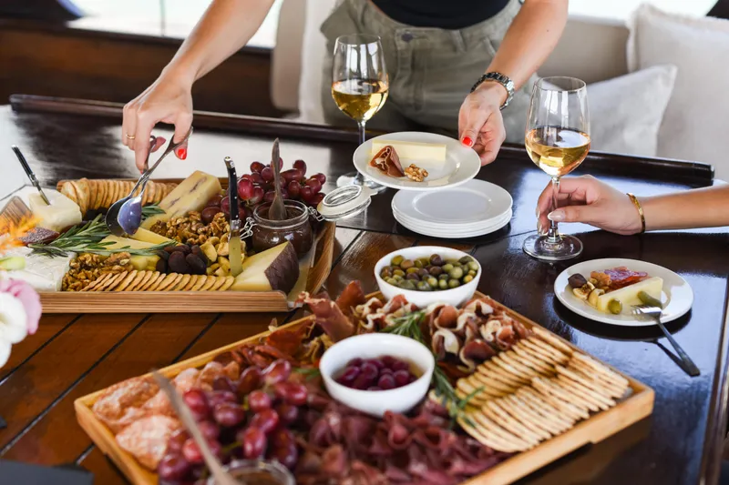 Gaiole Yacht Photos Pics Cheese and charcuterie board with wine, grapes, olives, and crackers on a wooden table.
