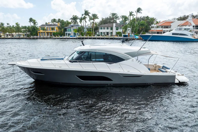 Sapphire Yacht Photos Pics 2022 Riviera 575 SUV yacht on water, surrounded by waterfront homes and palm trees.