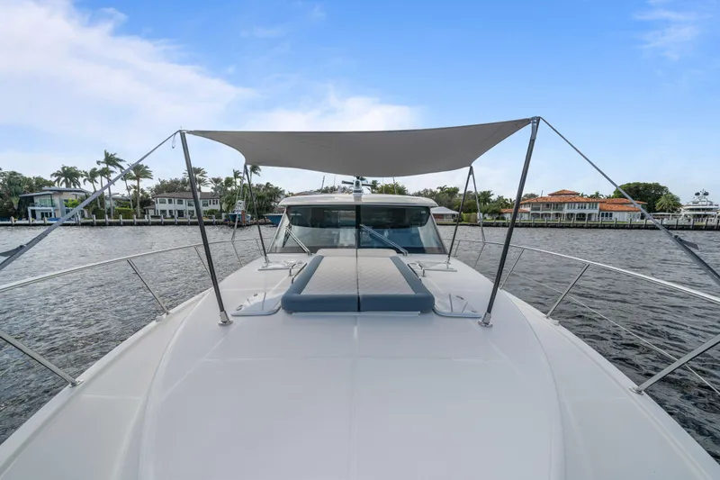 Sapphire Yacht Photos Pics 2022 Riviera 575 SUV yacht with sunshade on calm water, luxury waterfront homes in background.