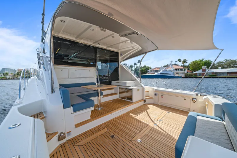 Sapphire Yacht Photos Pics Luxurious 2022 Riviera 575 SUV yacht with spacious deck and seating, docked by waterfront homes.