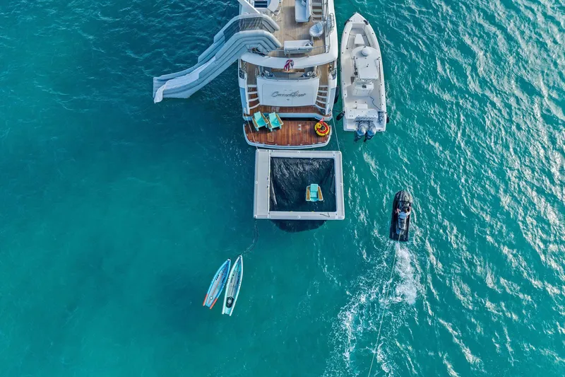 Current Sea Yacht Photos Pics Aerial view of 2011 Princess 95 yacht with slide, paddleboards, and jet ski in turquoise water.