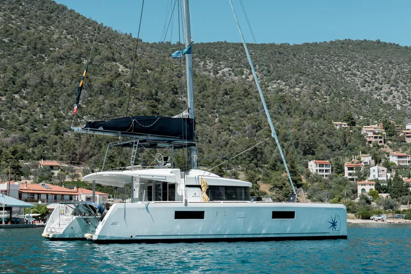 Yacht Photos Pics 2018 Lagoon 52 F catamaran sailing near a coastal village with lush hills.
