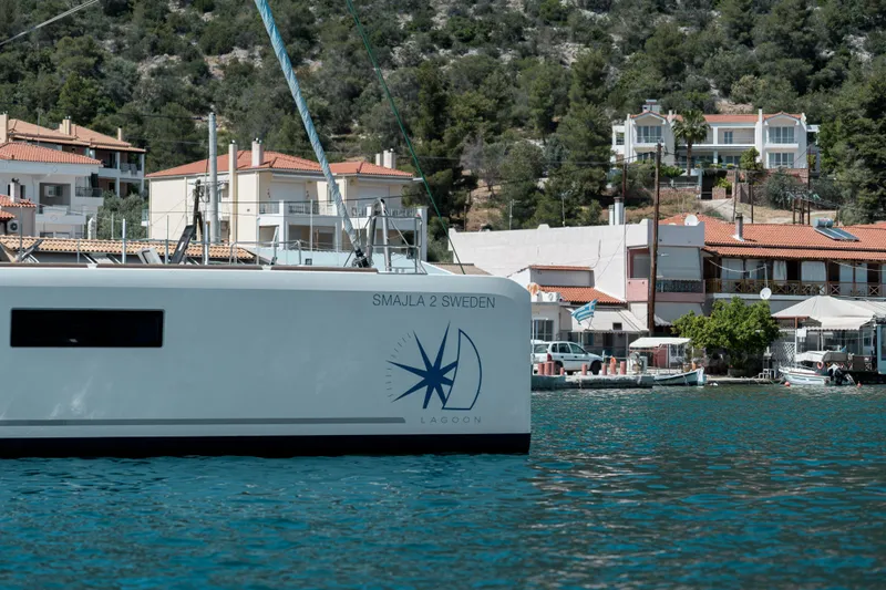  Yacht Photos Pics 2018 Lagoon 52 F catamaran docked near coastal village with hillside houses.