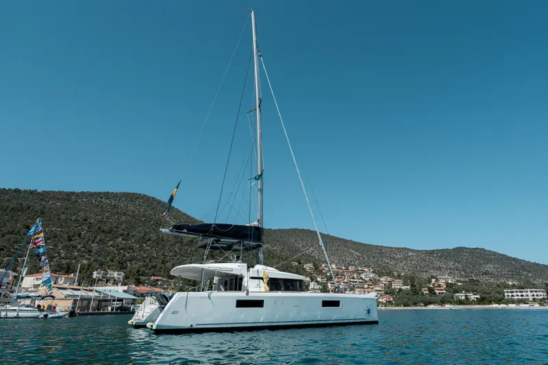  Yacht Photos Pics 2018 Lagoon 52 F catamaran sailing near coastal town with hills in background.