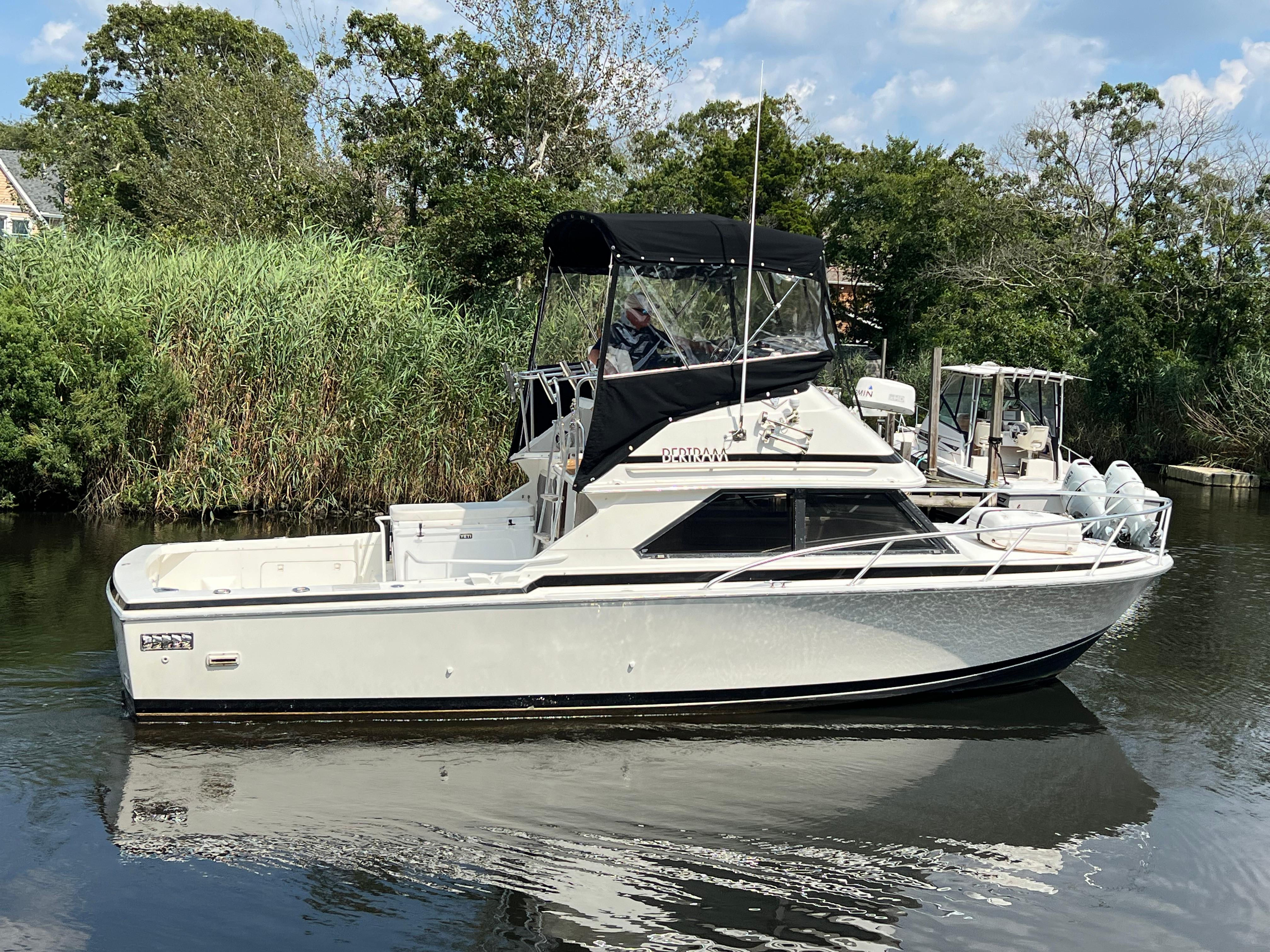 1990 Bertram 28 Flybridge boat on calm water, surrounded by lush greenery.