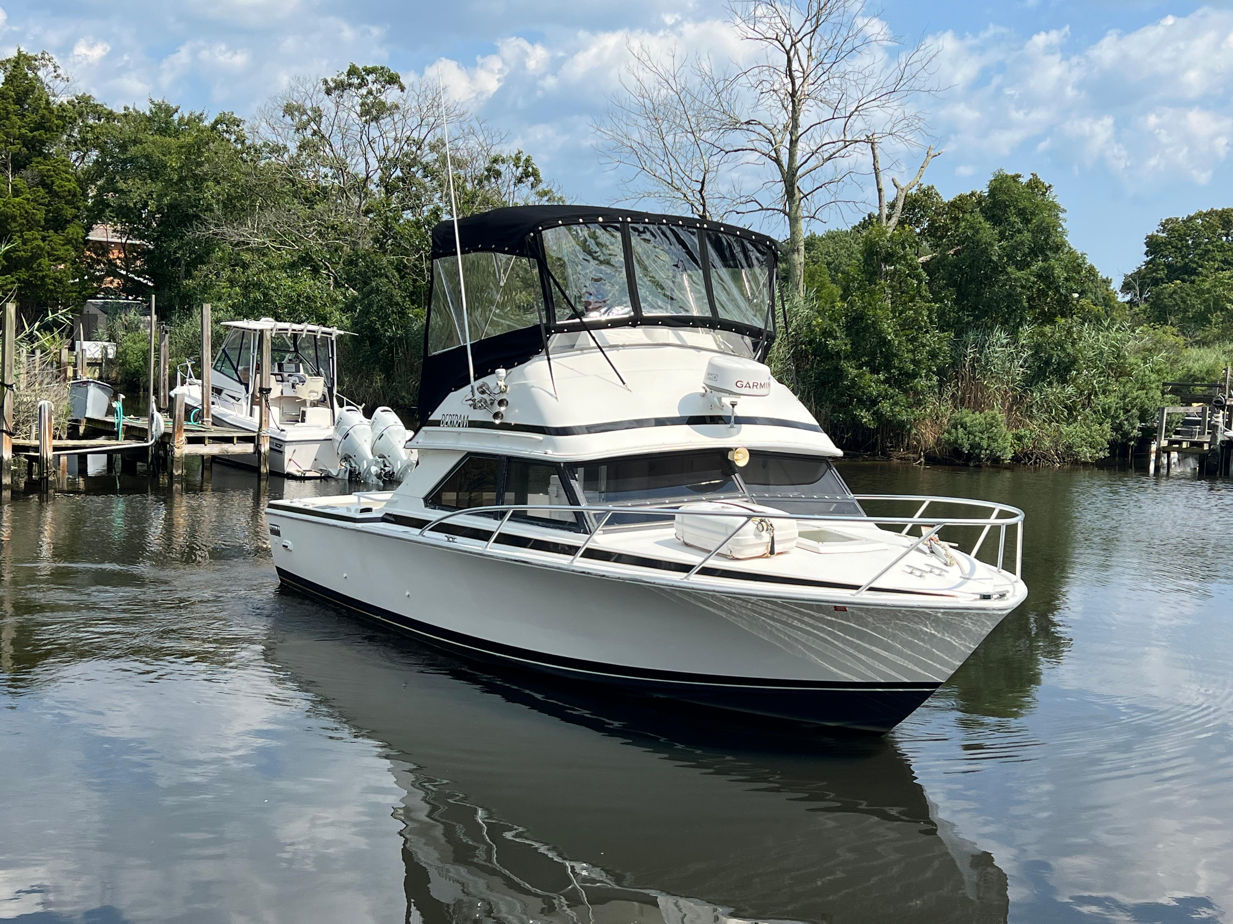 1990 Bertram 28 Flybridge boat on a calm river, surrounded by lush greenery.