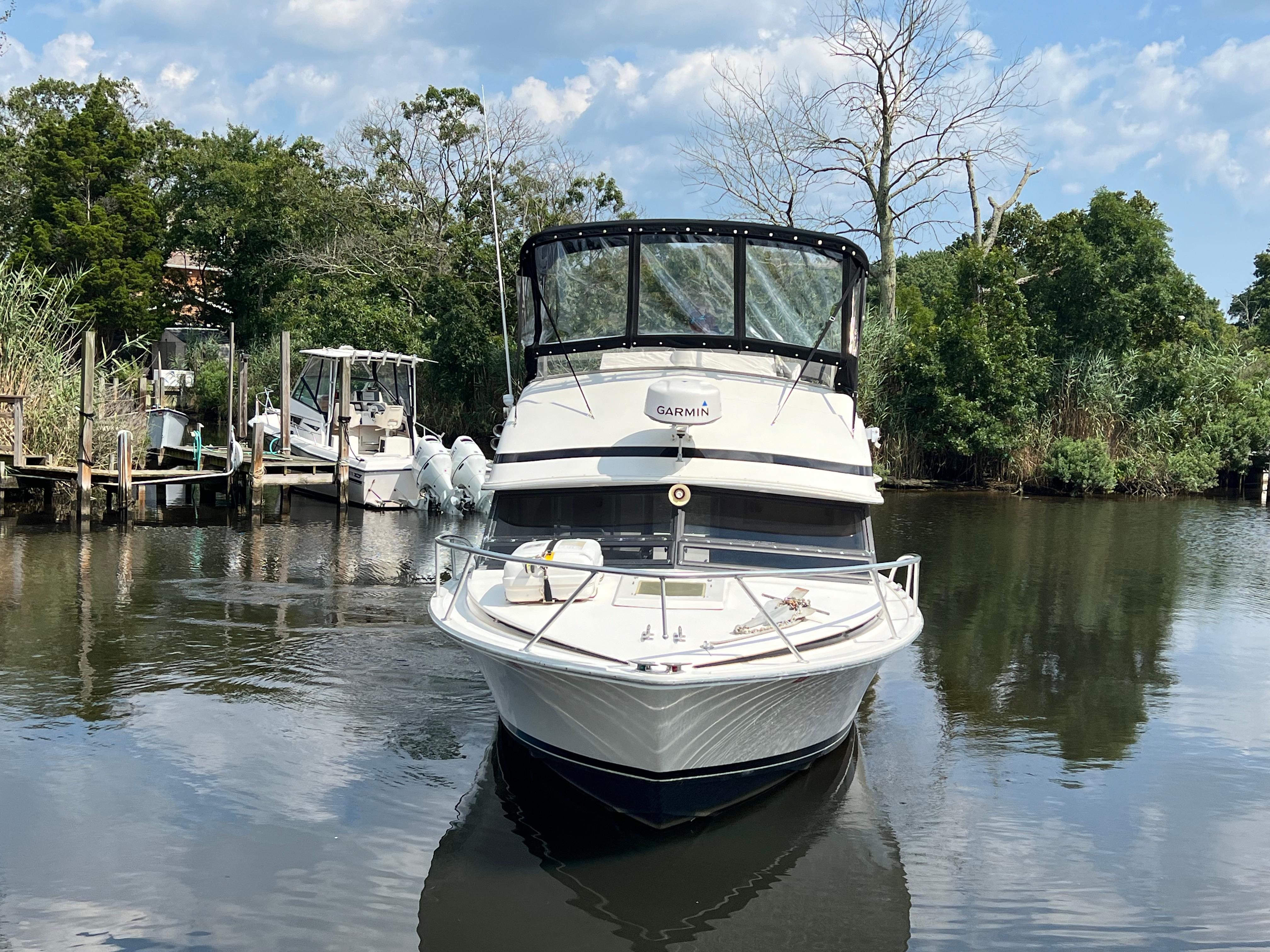 1990 Bertram 28 Flybridge boat on calm water, surrounded by lush greenery.