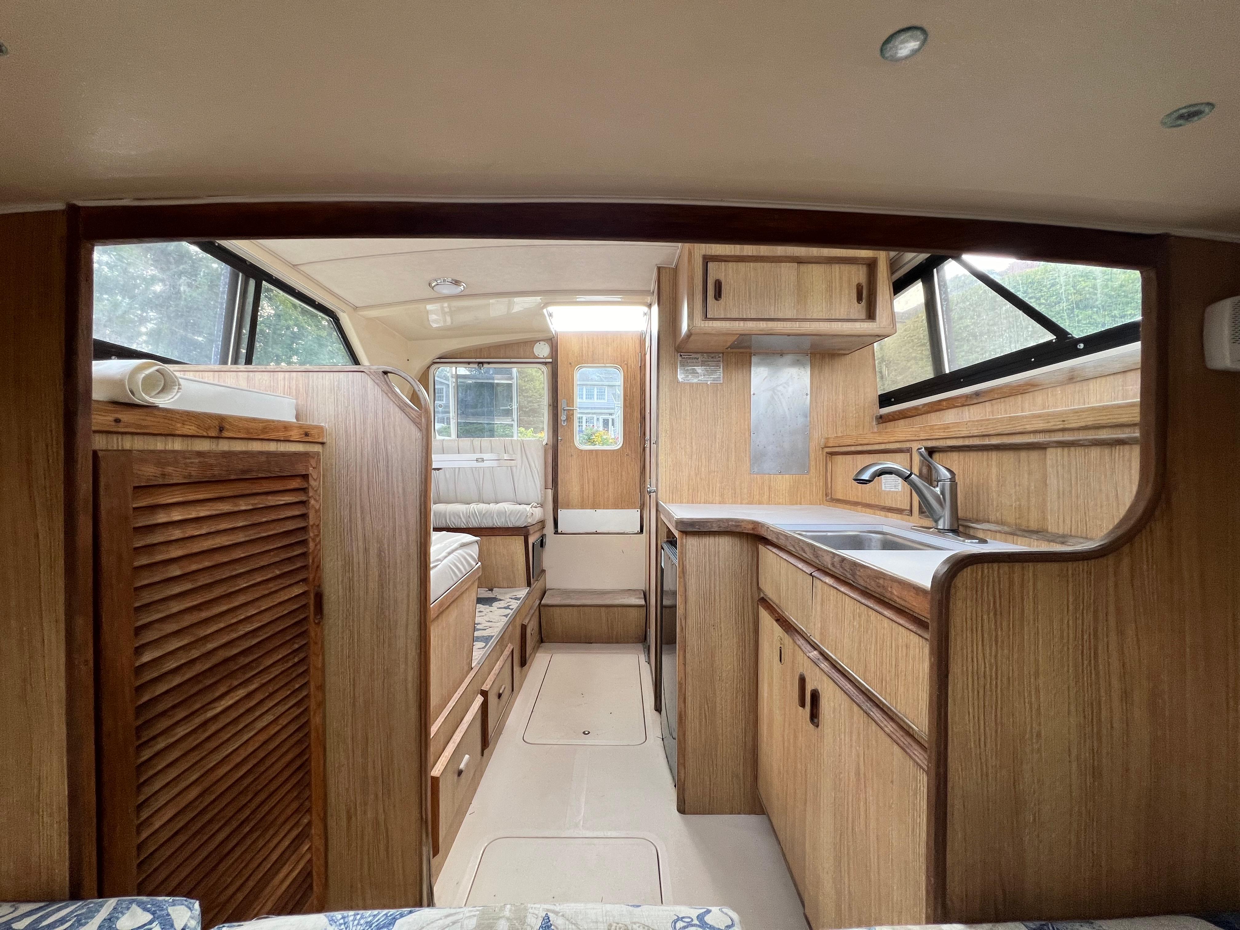 Interior of a 1990 Bertram 28 Flybridge boat with wood cabinetry and compact kitchen area.