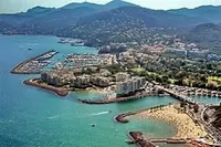Aerial view of coastal town with marina, beaches, and mountains in the background, 2023.