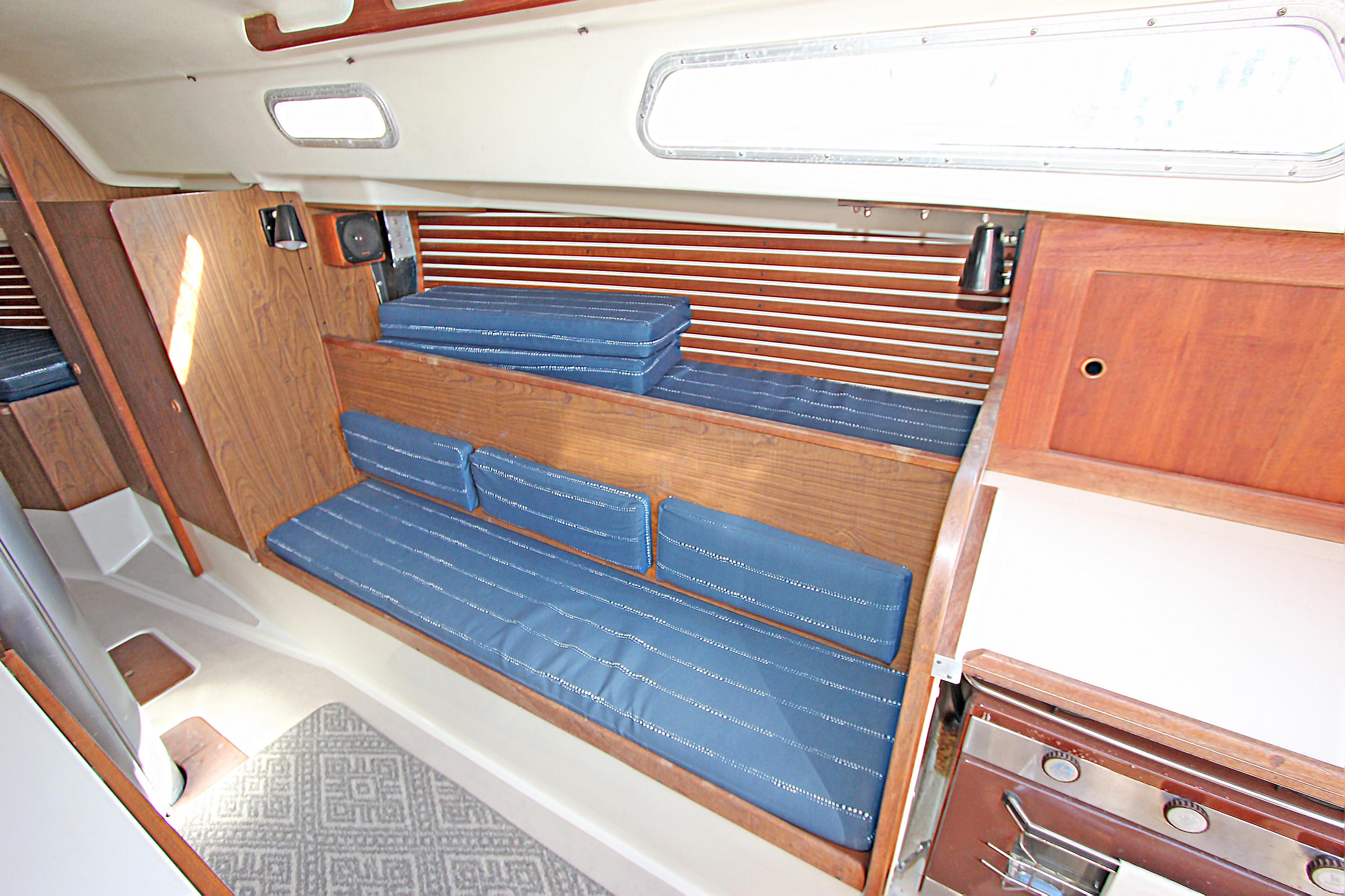 Interior of a 1977 Pearson 10M sailboat with blue cushioned seating and wooden accents.