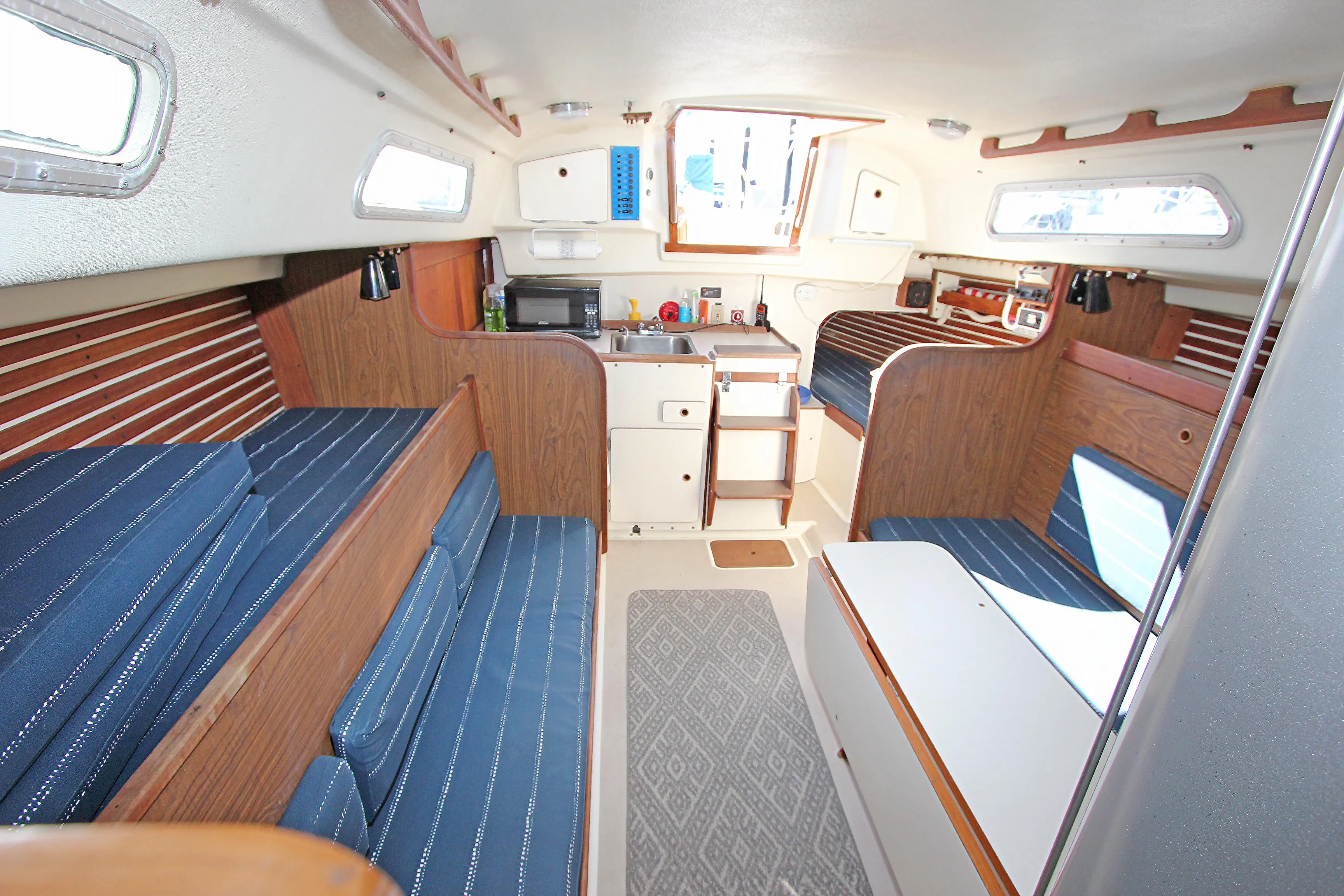 Interior of a 1977 Pearson 10M sailboat with blue seating and wooden accents.