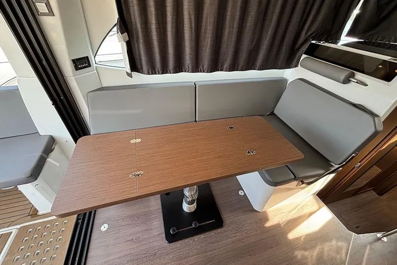  Yacht Photos Pics Interior of 2023 Beneteau Antares 11, featuring a wooden table and gray seating.