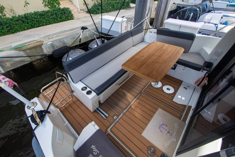 Sea Scape Yacht Photos Pics 2021 Jeanneau NC 1095 boat deck with seating and wooden table, docked at marina.