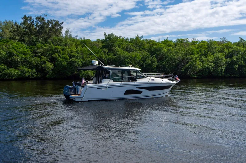 Sea Scape Yacht Photos Pics 2021 Jeanneau NC 1095 boat cruising on a calm river with lush greenery.