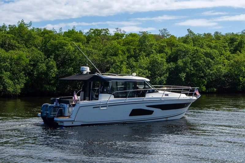 Sea Scape Yacht Photos Pics 2021 Jeanneau NC 1095 boat cruising on a calm river with lush greenery.