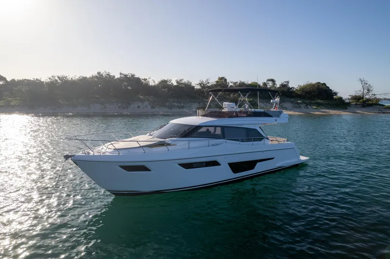  Yacht Photos Pics 2023 Ferretti Yachts 500 cruising on serene waters near a wooded shoreline.