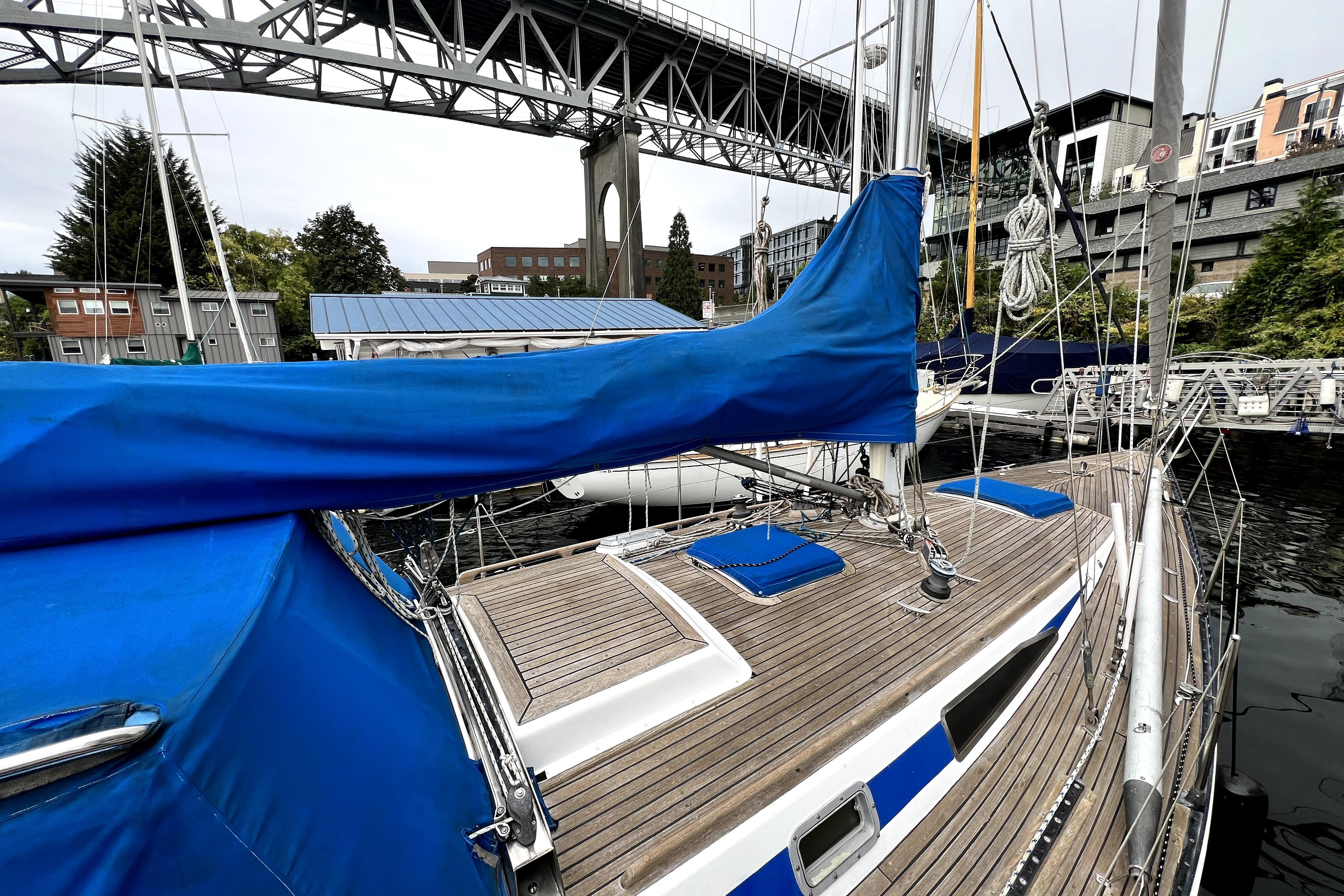 1983 CT 38 Warwick sailboat docked under a bridge, featuring blue covers and wooden deck.
