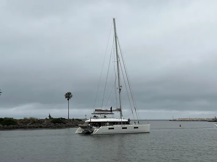 Sunset O Yacht Photos Pics 2019 Lagoon 620 catamaran sailing in a calm harbor under cloudy skies.