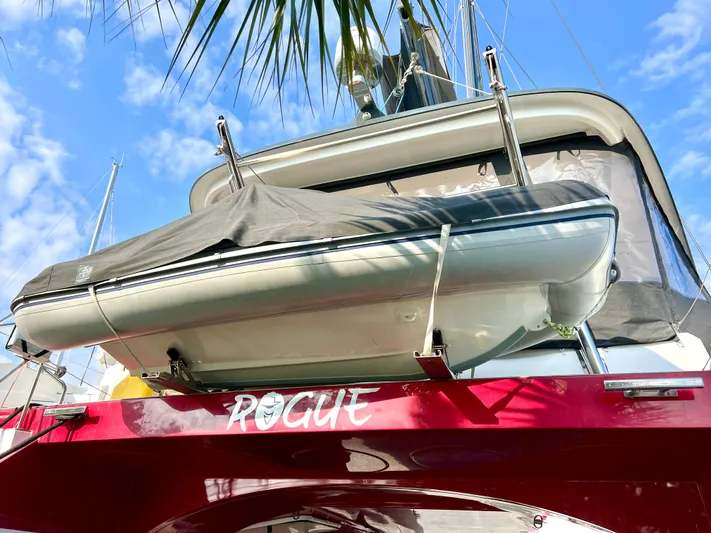 Rogue Yacht Photos Pics Red Privilege 510 yacht with covered dinghy, palm leaves, and blue sky background.