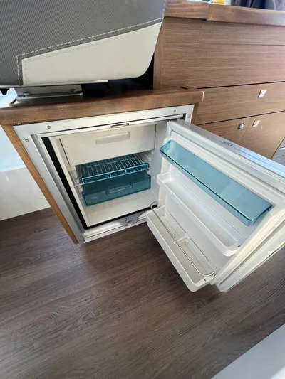  Yacht Photos Pics 2021 Jeanneau 895 boat interior with open refrigerator and wooden cabinetry.