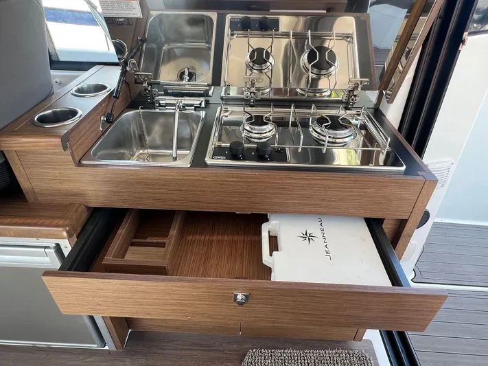  Yacht Photos Pics 2021 Jeanneau 895 boat kitchen with dual-burner stove, sink, and storage drawers.