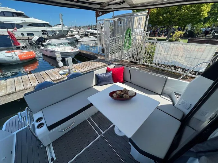  Yacht Photos Pics Jeanneau 895 2021 model boat with a cozy seating area and table at the dock.