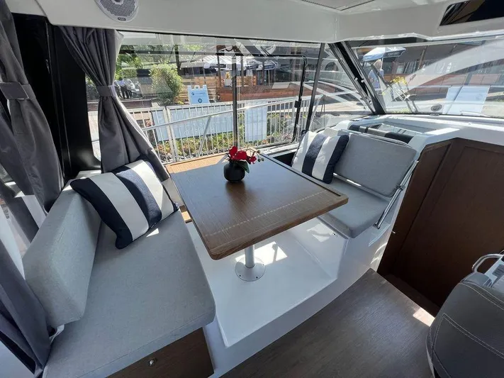  Yacht Photos Pics Interior of 2021 Jeanneau 895 boat with dining area, striped cushions, and large windows.