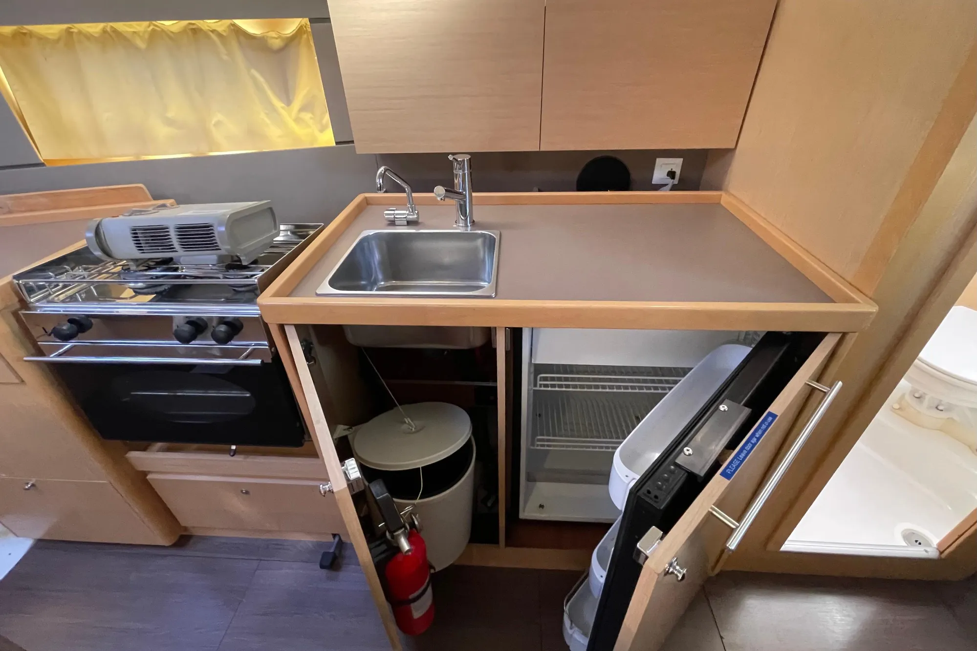 Compact kitchen area in a 2015 Beneteau First 235 sailboat, featuring a sink, stove, and fridge.