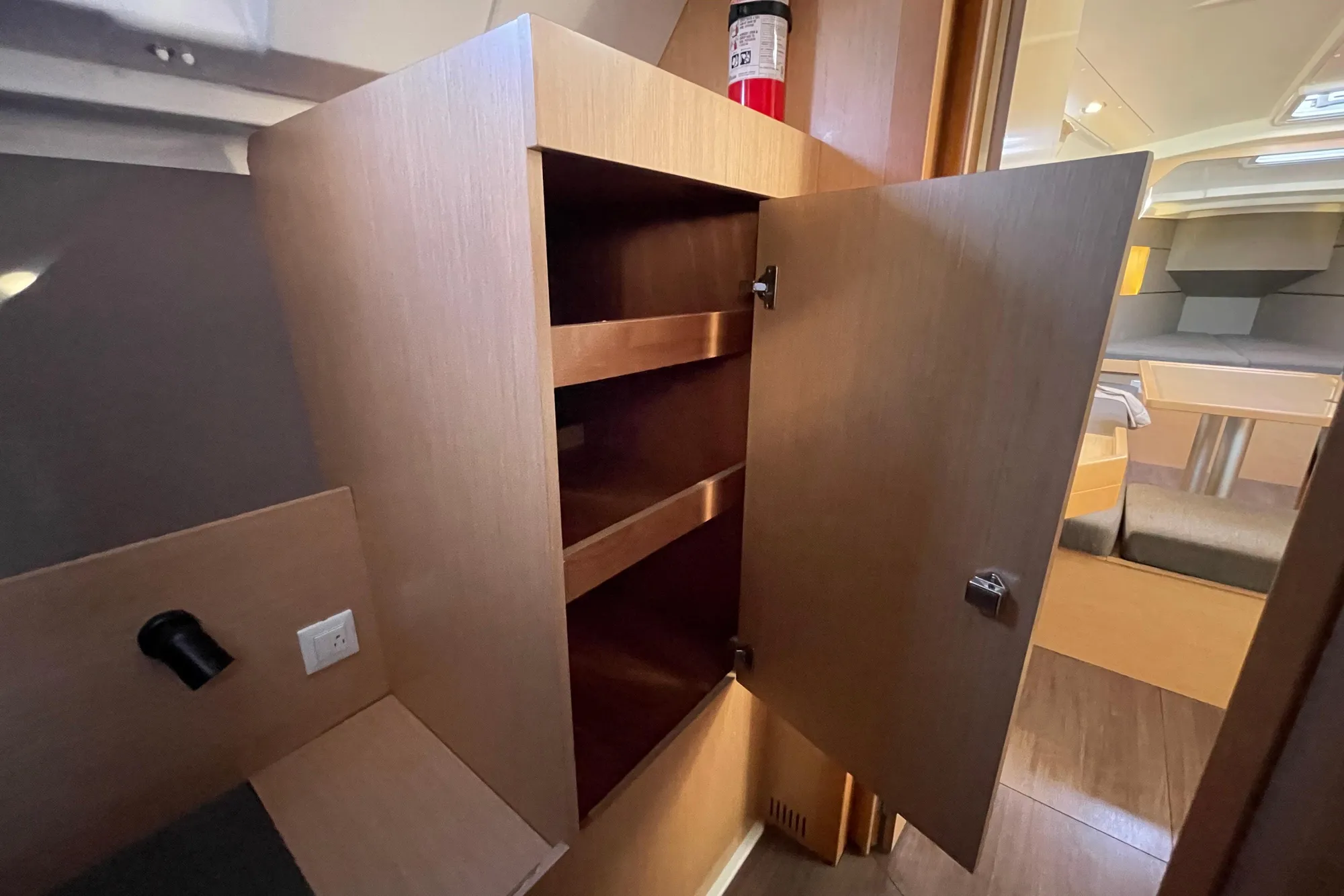 Interior of 2015 Beneteau First 235 sailboat with open wooden cabinet and fire extinguisher.