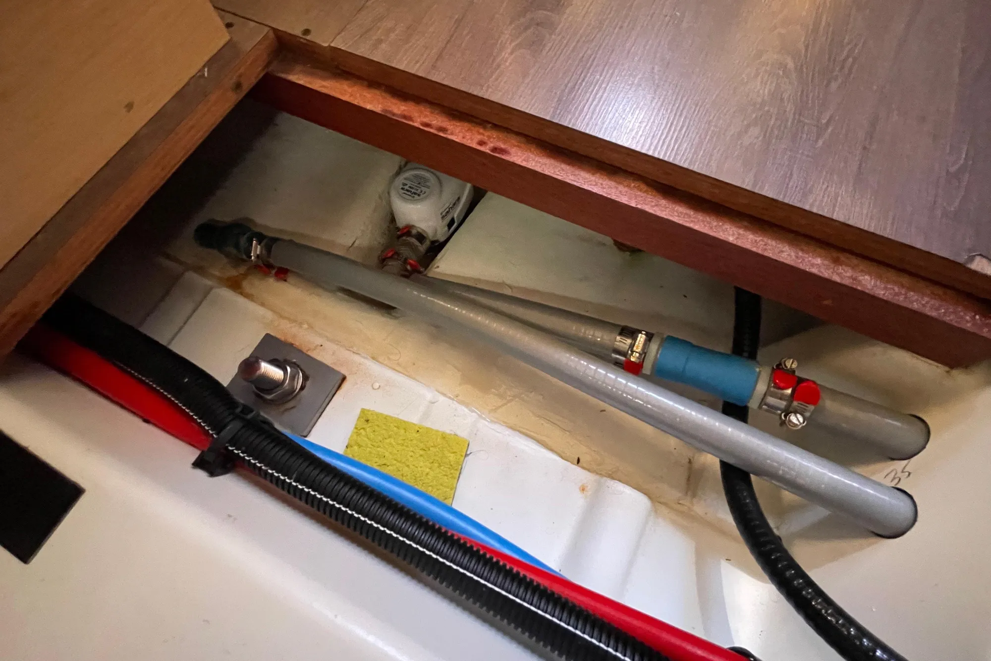 Bilge area of 2015 Beneteau First 235 sailboat showing plumbing and wiring.
