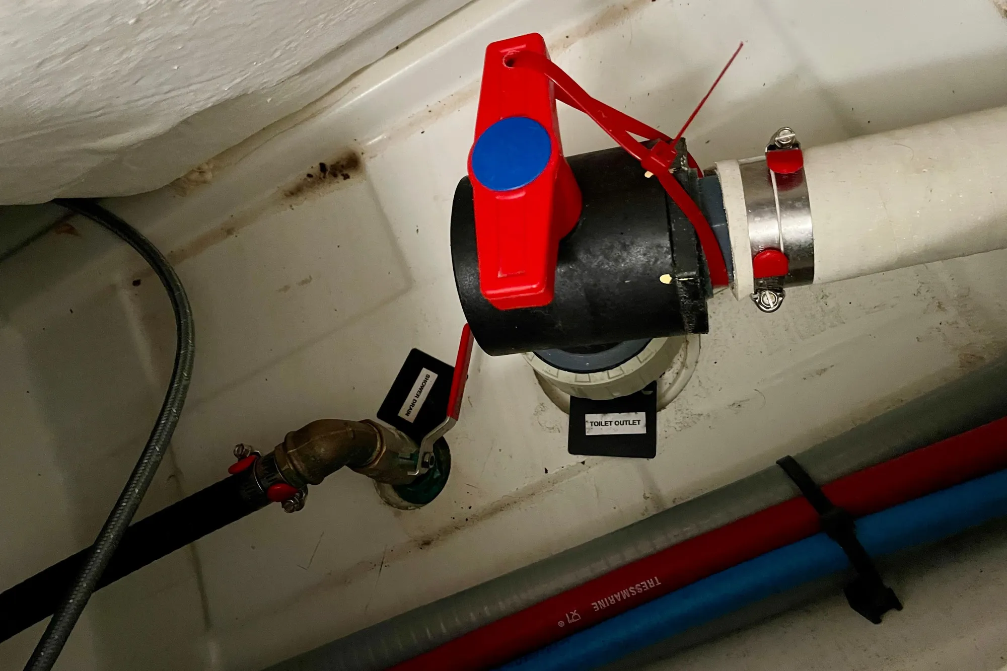 Boat plumbing system with red valve, labeled "Toilet Outlet," in a 2015 Beneteau First 235.