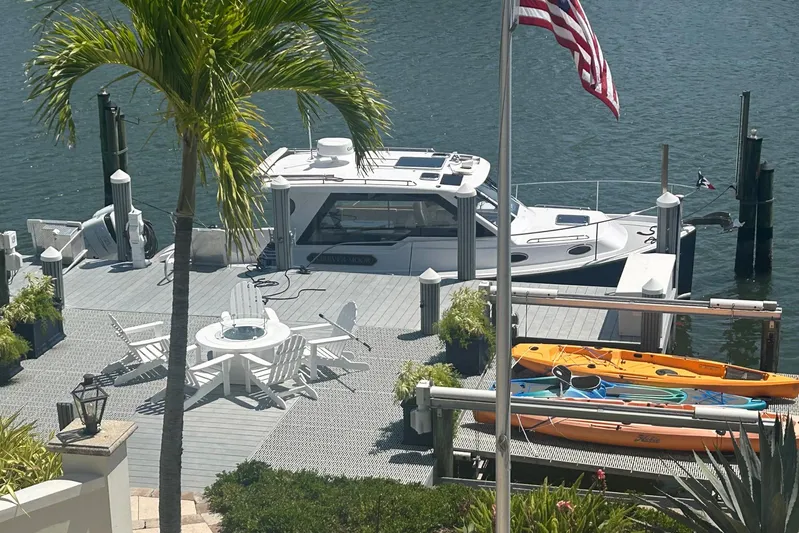 Forever Moor Yacht Photos Pics 2024 True North 34 Outboard Express docked by a waterfront patio with kayaks and palm trees.