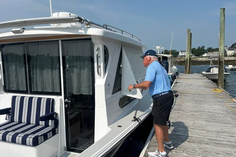 Forever Moor Yacht Photos Pics Man adjusting curtain on 2024 True North 34 Outboard Express boat docked at marina.
