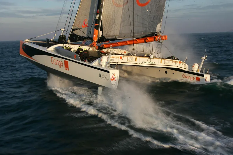 Vitalia II Yacht Photos Pics High-performance 2003 Multiplast catamaran sailing swiftly on open water, branded with "Orange."
