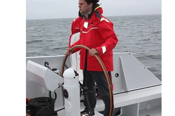 Vitalia II Yacht Photos Pics Person steering a 2003 Multiplast High Performance Catamaran in red jacket on open water.