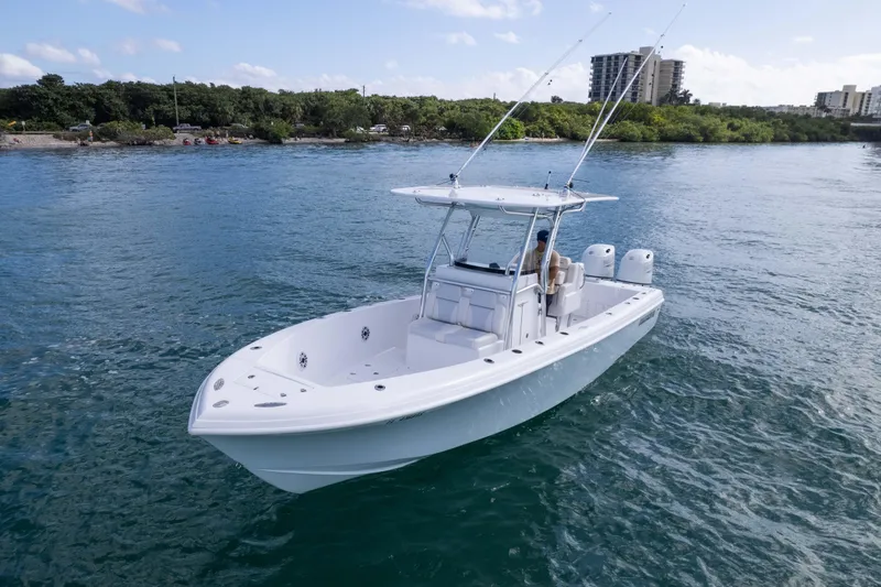  Yacht Photos Pics 2024 Bluewater 2550 boat on calm water, surrounded by lush greenery and distant buildings.