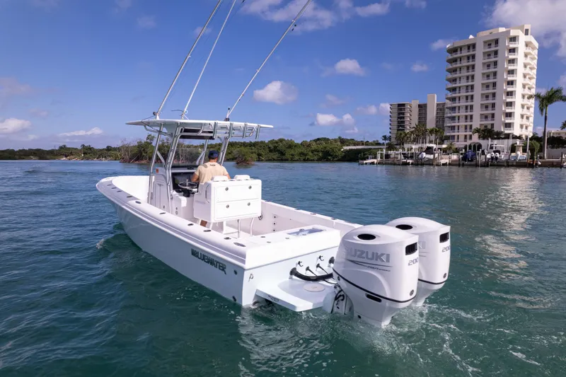  Yacht Photos Pics 2024 Bluewater 2550 boat with dual Suzuki engines cruising near waterfront buildings.