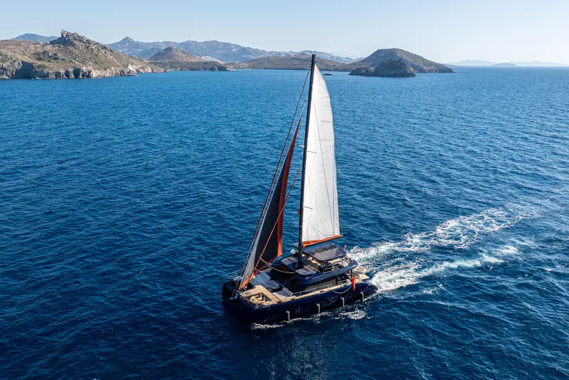  Yacht Photos Pics 2024 Sunreef 60 Eco catamaran sailing in clear blue waters near rocky islands.