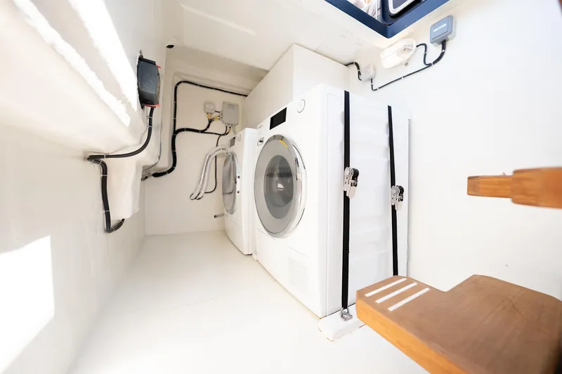  Yacht Photos Pics Laundry area inside 2024 Sunreef 60 Eco yacht, featuring washing machine and wooden steps.