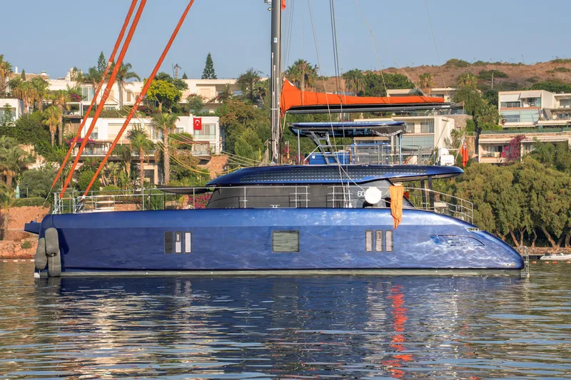  Yacht Photos Pics 2024 Sunreef 60 Eco yacht in vibrant blue, docked near luxury waterfront homes.
