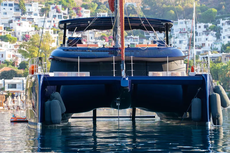  Yacht Photos Pics 2024 Sunreef 60 Eco catamaran docked in a scenic harbor with hillside buildings.