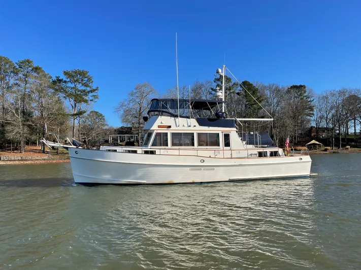 30 West Yacht Photos Pics 1991 Grand Banks 49 Classic yacht on calm water, surrounded by trees.