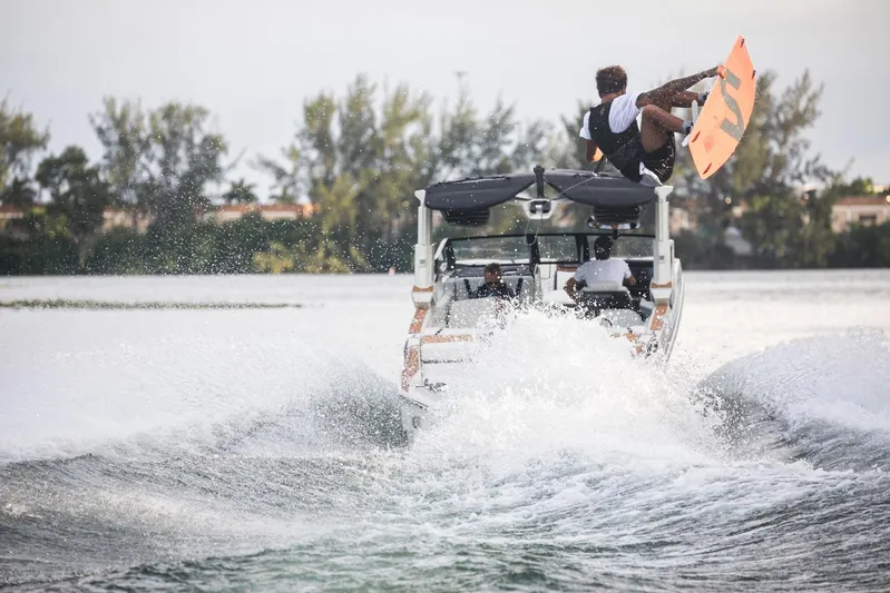  Yacht Photos Pics Wakeboarder jumps behind 2025 Nautique Super Air Nautique G25 Paragon on a lake.