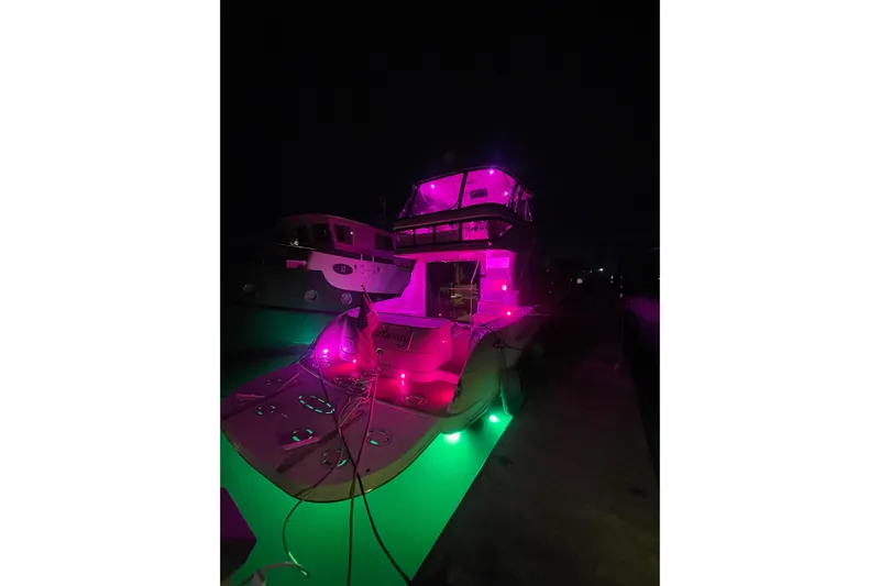 Low Hours! Yacht Photos Pics 2006 Sea Ray 580 Sedan Bridge yacht illuminated with vibrant pink and green lights at night.